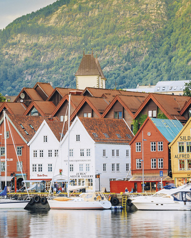 Bunte Holzhäuser und Boote am Hafen vor einer Bergkulisse.