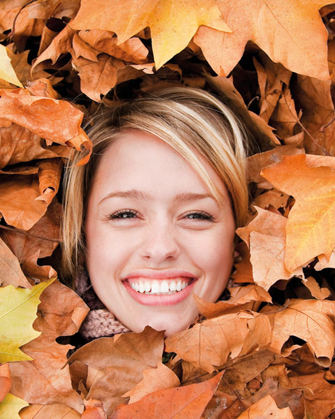 Lächelndes Gesicht einer Frau, umgeben von bunten Herbstblättern.