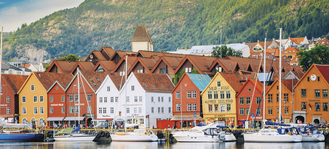 Bunte Holzhäuser und Boote am Hafen vor einer Bergkulisse.