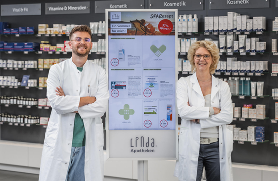 Eine LINDA Apothekerin und ein LINDA Apotheker lehnen sich rechts und links an das LINDA ePoster, das das LINDA SPARezept zeigt