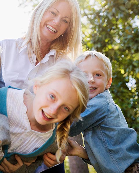 Eine blonde Frau mit vier blonden Kindern, die in der Sonne an einem Ort mit Bäumen lachen.