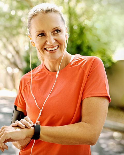  Eine Frau in einem orangefarbenen T-Shirt lächelt, während sie Musik über ihre Kopfhörer hört.