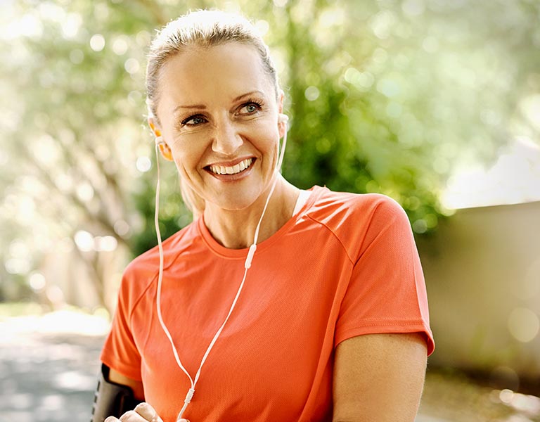 Eine Frau in einem orangefarbenen T-Shirt lächelt, während sie Musik über ihre Kopfhörer hört.